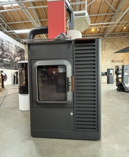 Moderner schwarzer Holzofen mit Glasfront und Metalldetails, ausgestellt in einem geräumigen Ausstellungsraum mit industriellem Dekor.