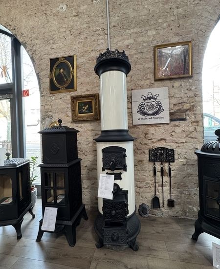 Ein eleganter weiß-schwarzer Vintage-Ofen steht in einem gemütlichen Ausstellungsraum, der mit verschiedenen gerahmten Kunstwerken geschmückt ist.