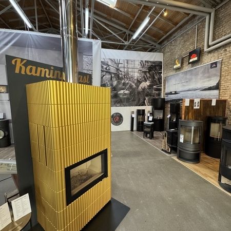 Ein moderner Ausstellungsraum mit einem leuchtend gelb gestreiften Holzofen mit Glasfront, umgeben von verschiedenen stilvollen Heizlösungen.
