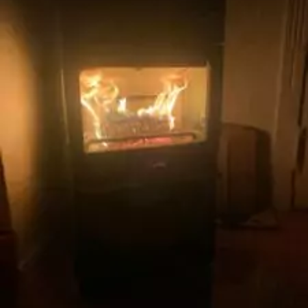 Ein flackerndes Feuer brennt in einem modernen schwarzen Ofen, der warmes Licht in einen schwach beleuchteten Raum wirft.