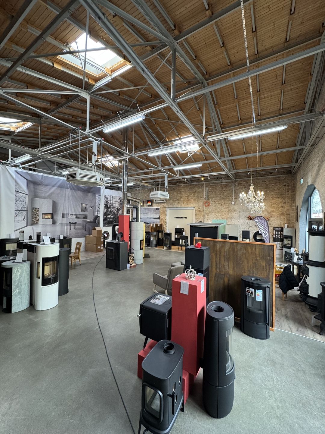 Ein geräumiger Innenraum mit hohen Decken, in dem eine Vielzahl von dekorativen Öfen, Geräten und Möbeln in einem stilvollen Ausstellungsraum präsentiert wird.