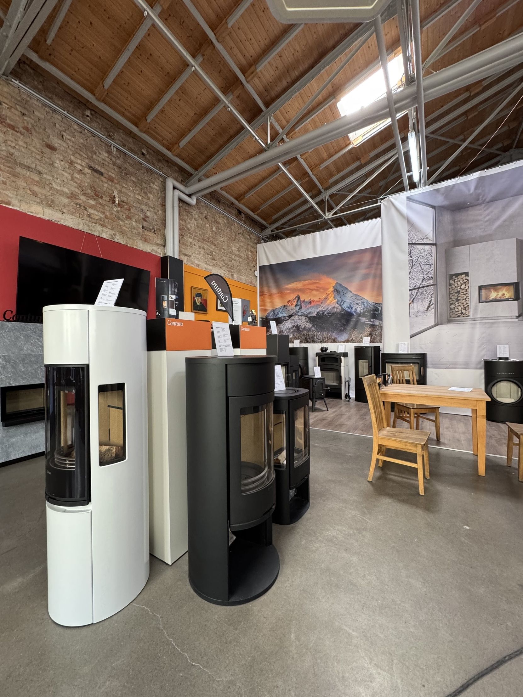 Eine Ausstellung moderner Holzöfen in einem Ausstellungsraum mit schwarz-weißem Design vor lebhaften Werbekulissen.
