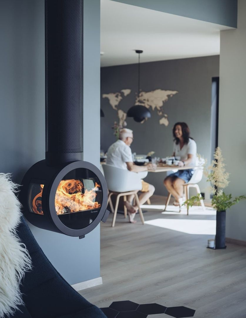 Ein moderner Wohnbereich mit einem stilvollen schwarzen Kamin mit sichtbaren Flammen, warmen Sitzgelegenheiten und einem Essbereich im Hintergrund.