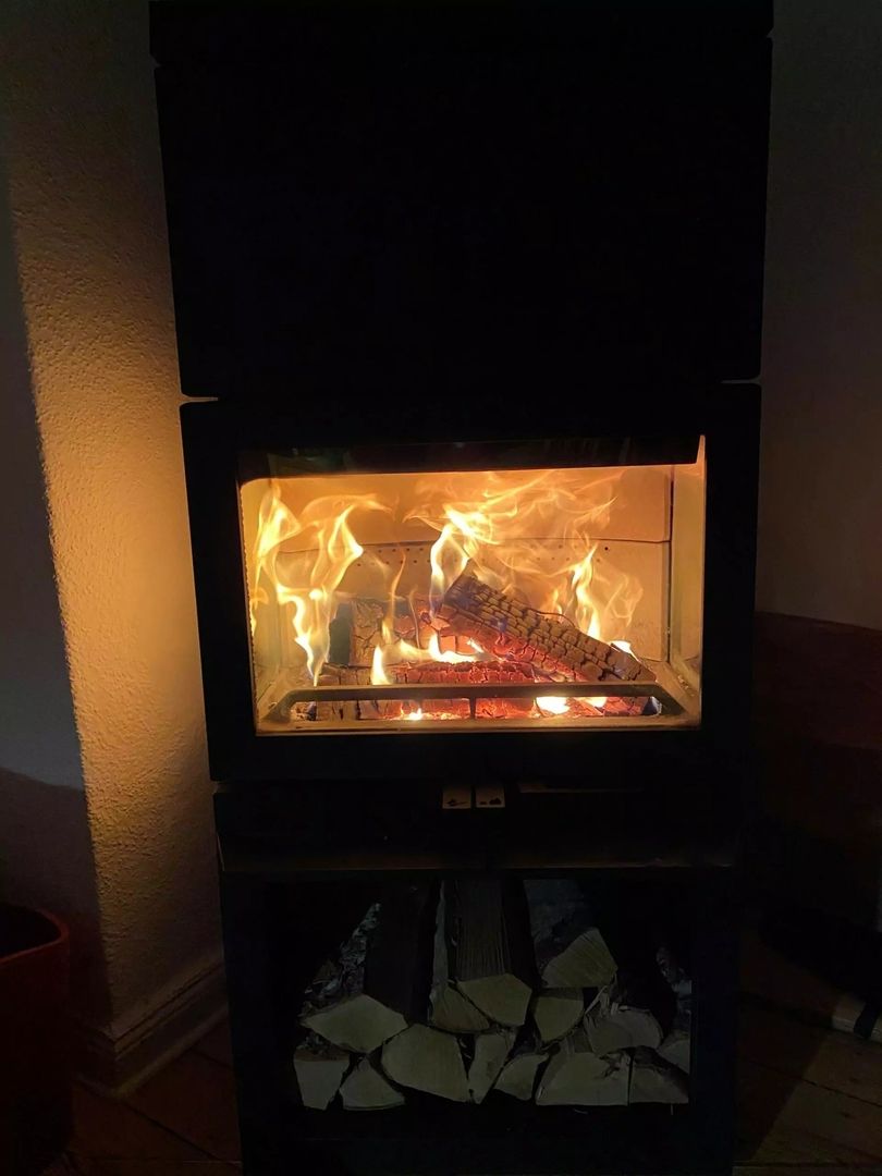 Ein flackerndes Feuer brennt in einem modernen schwarzen Ofen, der warmes Licht in einen schwach beleuchteten Raum wirft.